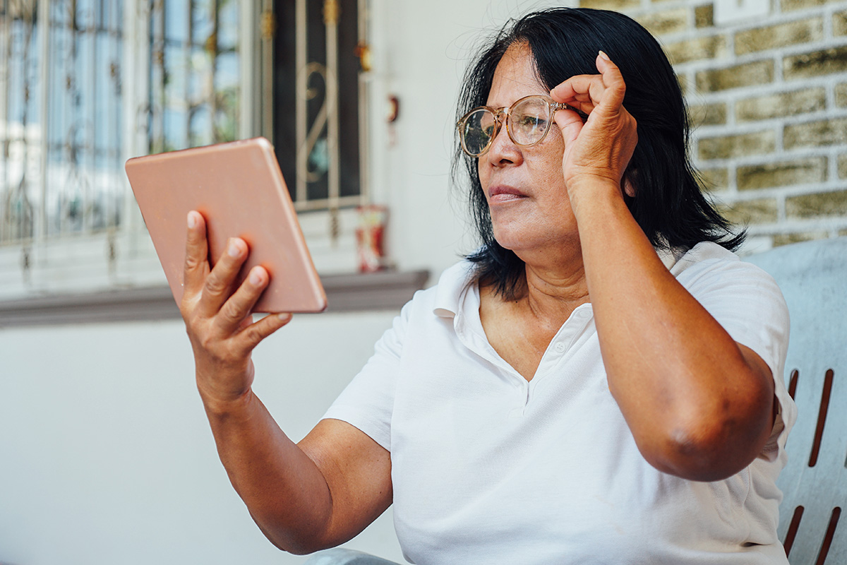 Woman looking at an iPad adjusting her glasses
